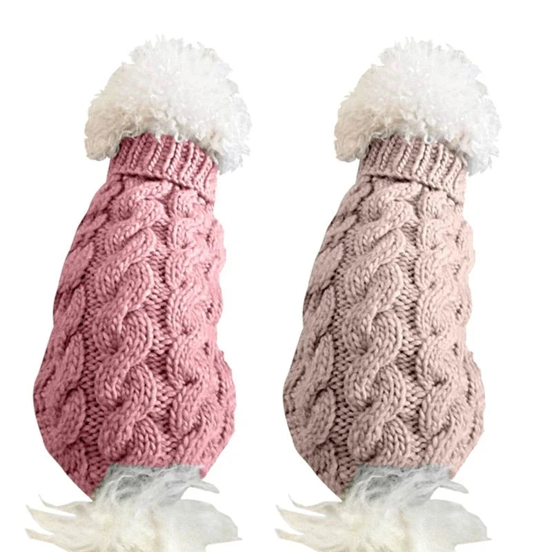Suéter tejido de cuello alto para perro en colores rosa y beige, con diseño de trenzas y pompones en la parte superior.