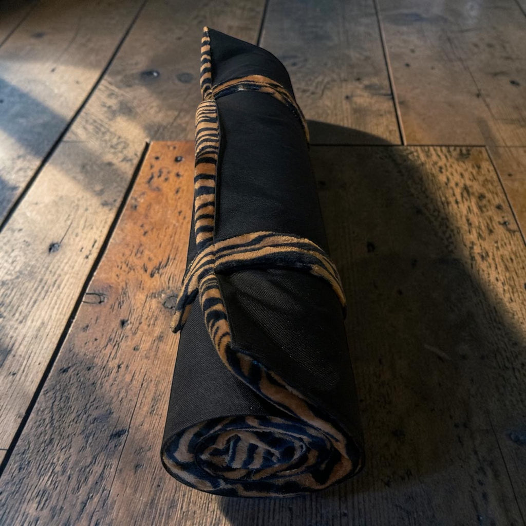 Colchoneta de voyage MITZON Tiger Edition enroulée, avec un motif tigre noir et doré, posée sur un sol en bois.