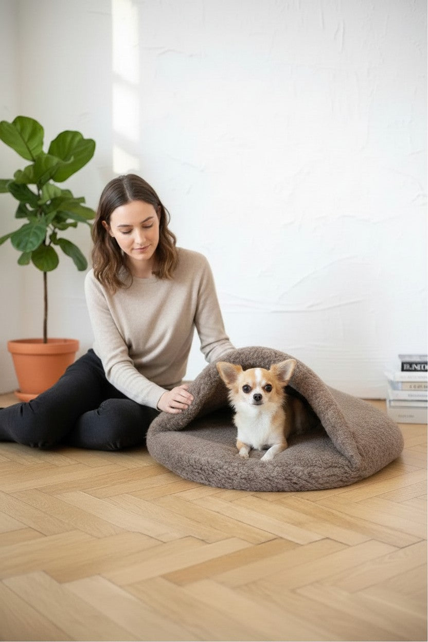 Femme assise près d'un petit chien dans une grotte pour animaux MITZON en laine beige artisanale sur parquet.