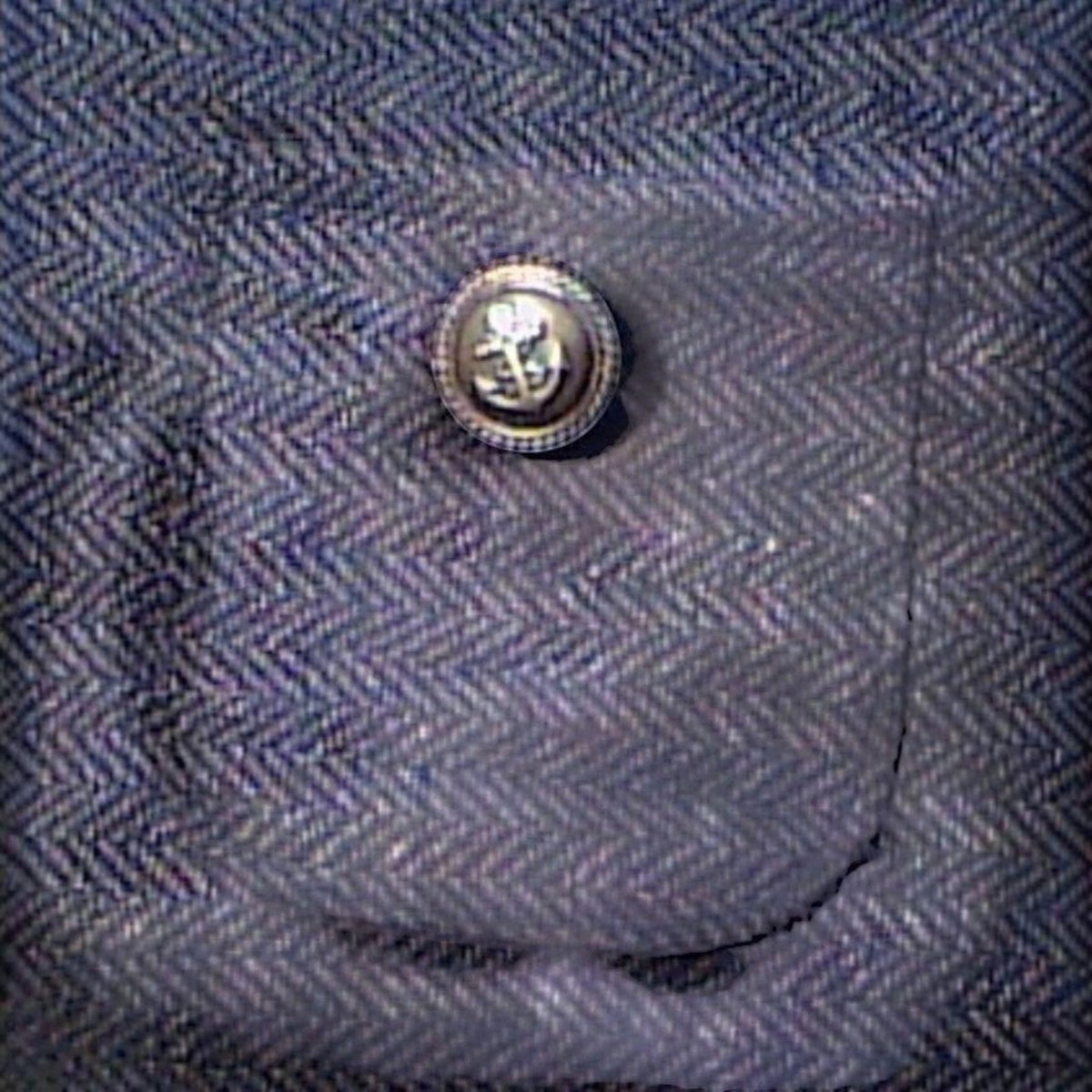 Gros plan sur le motif à chevrons marron du manteau pour chien MITZON avec une poche ornée d'un bouton blazer