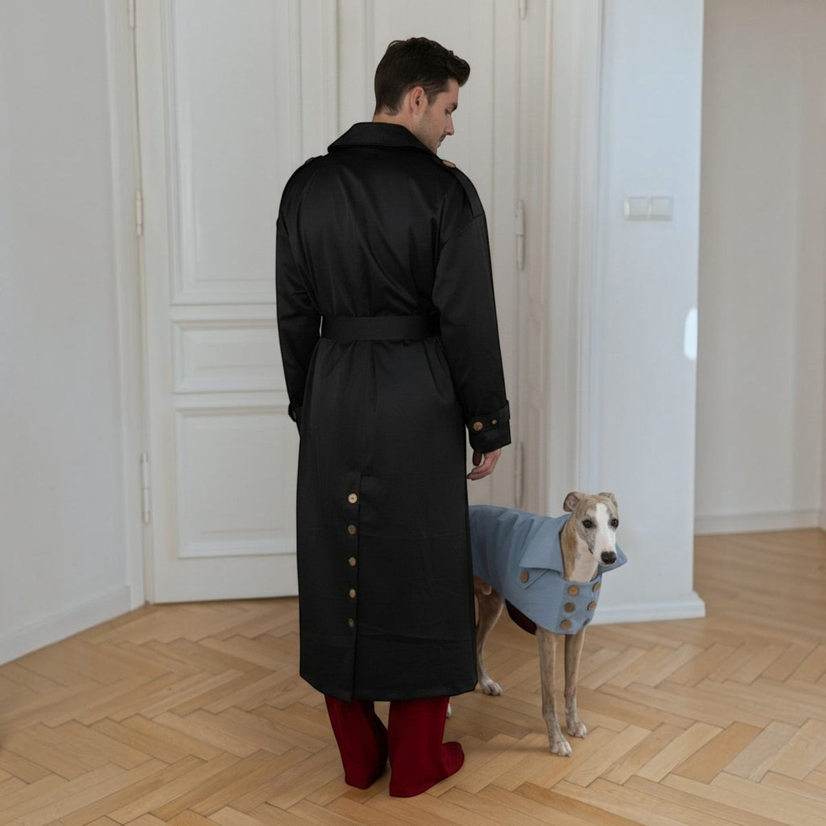 Chien portant un trench-coat MITZON bleu clair déperlant en coton avec boutons en noix de coco, à côté d'un homme.