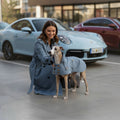 Chien portant un trench-coat MITZON bleu clair en coton déperlant avec boutons en noix de coco, aux côtés de sa propriétaire